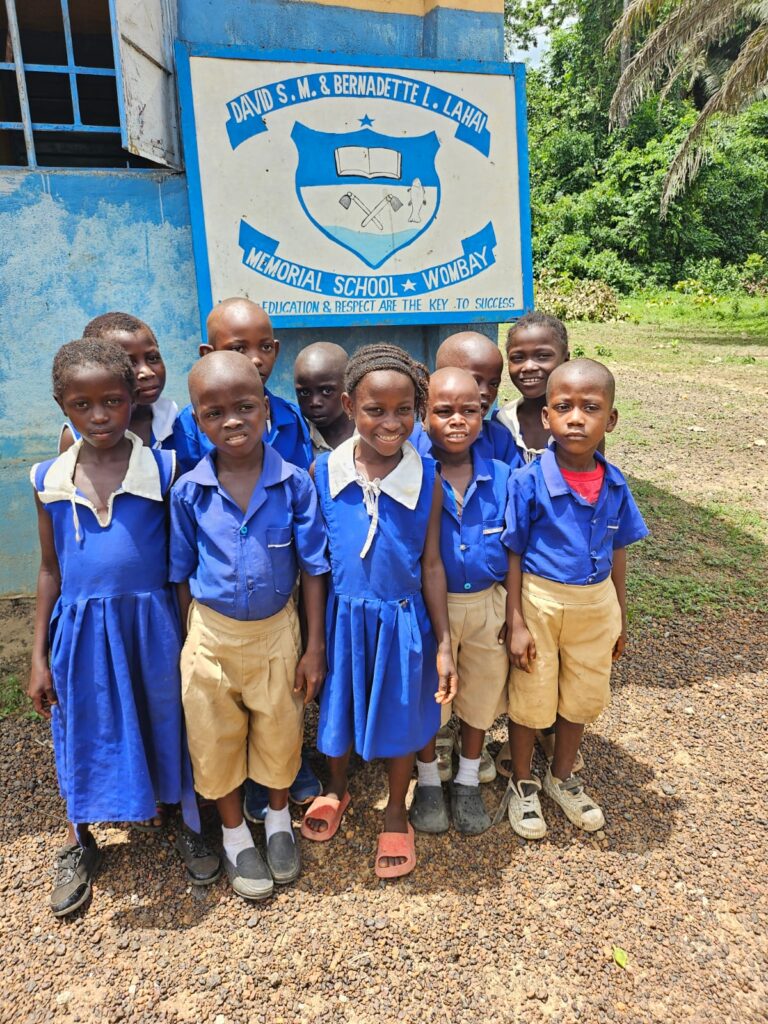 Lahai School Students A group of children in blue and khaki uniforms standing in front of a sign.